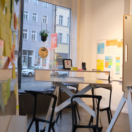 Whiteboards, Stehhocker und Tisch in einem hellen Raum mit großen Fenstern